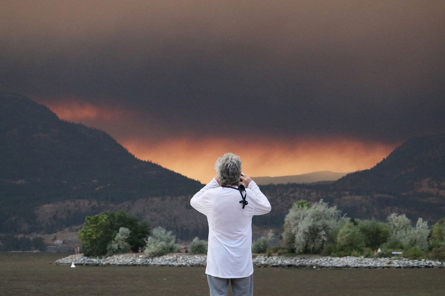 A man looks towards the White Rock Lake wildfire from downtown Kelowna, B.C., on Aug. 15, 2021. (Photo by Aaron Hemens for Kelowna Capital News)