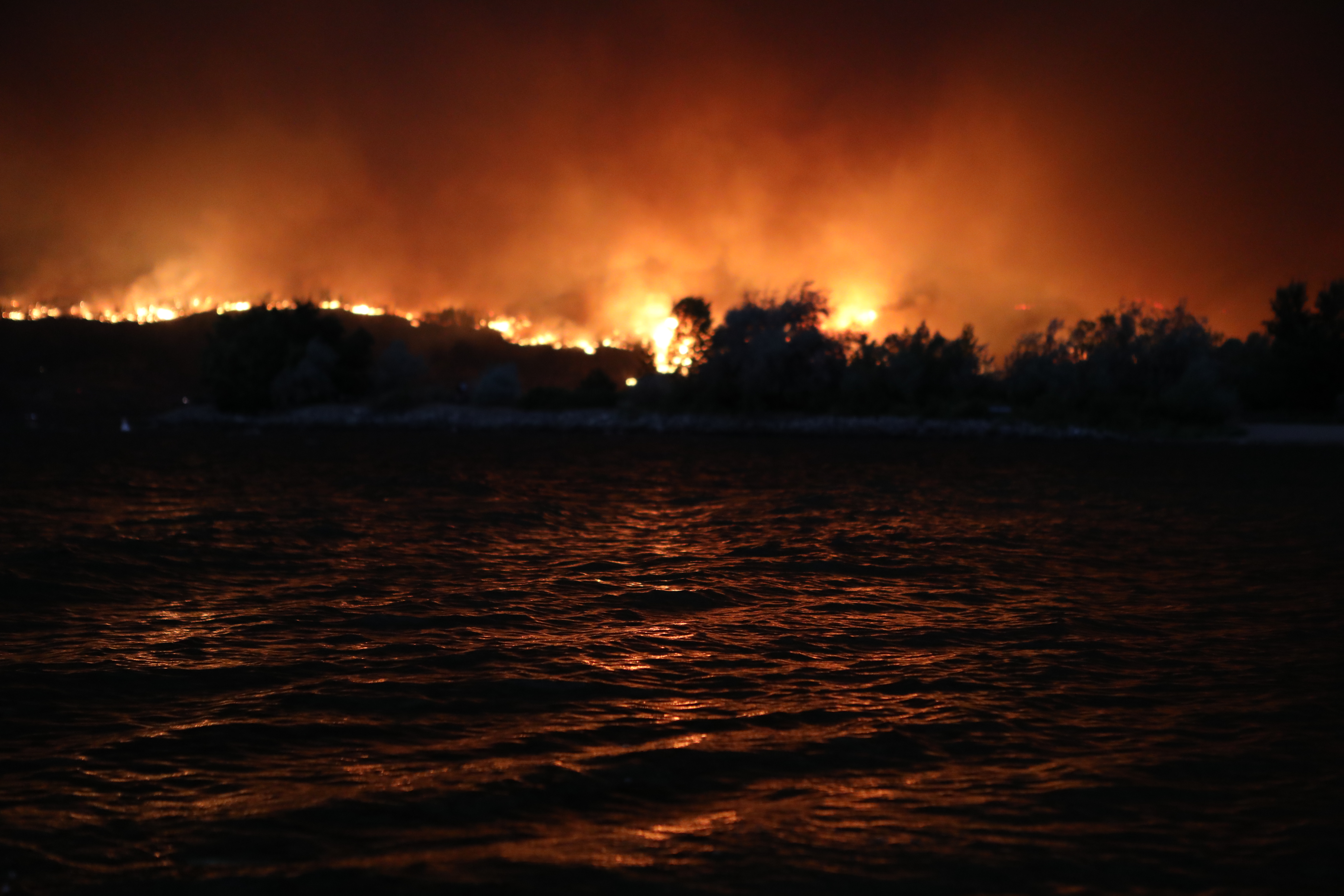 The McDougall Creek wildfire burning above the hills in West Kelowna, B.C., is reflected in Okanagan Lake on the evening of Aug. 17, 2023. The blaze, which measured at 1,100 hectares that same night, has resulted in thousands of evacuation alerts, and led to the the City of West Kelowna and parts of Westbank First Nation declaring a state of emergency that earlier that day. (Photo by Aaron Hemens for the Globe and Mail)
